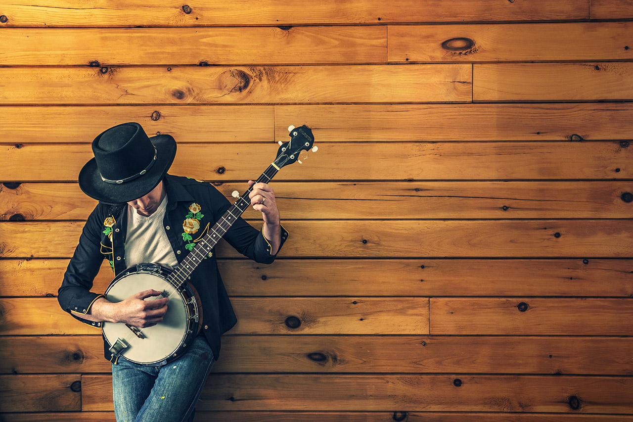 Man playing banjo against wooden wall.